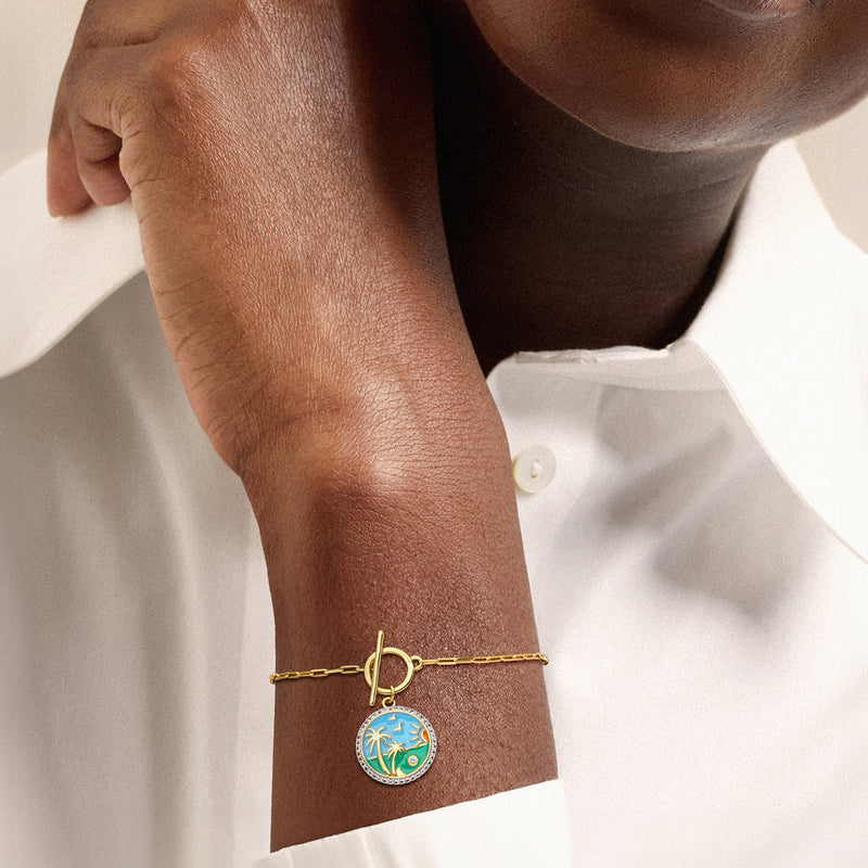 Gold-tone beach charm toggle bracelet on wrist, round blue enamel charm