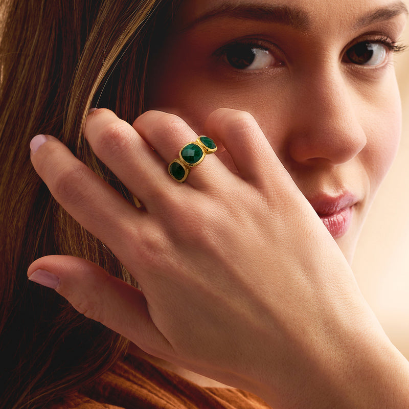 Emerald-green three-stone bezel ring on finger with gold-tone setting