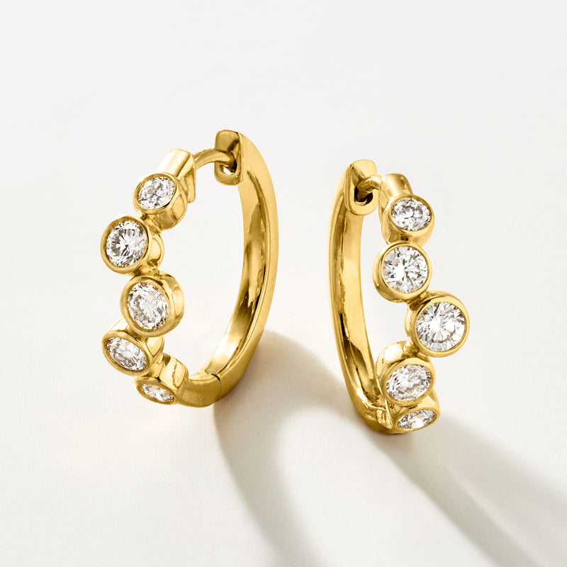 Gold hoop earrings with five round diamonds; bezel settings on a hinged hoop