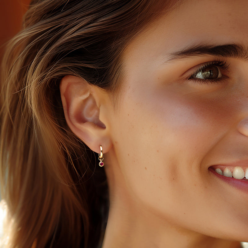 Ruby bezel hoop charm earrings on ear with small red gemstone drops