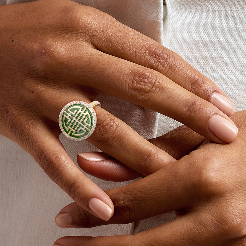 Gold-tone ring with green enamel oval motif and white stone halo on finger
