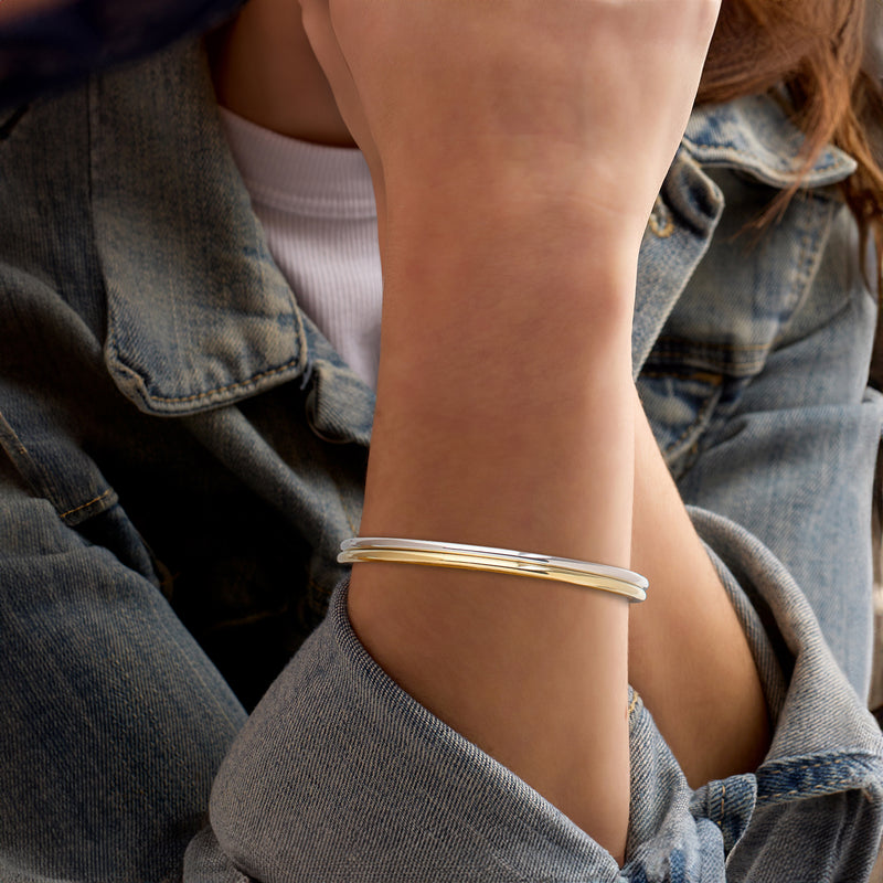 Two polished bangle bracelets worn on wrist, gold over silver two-tone