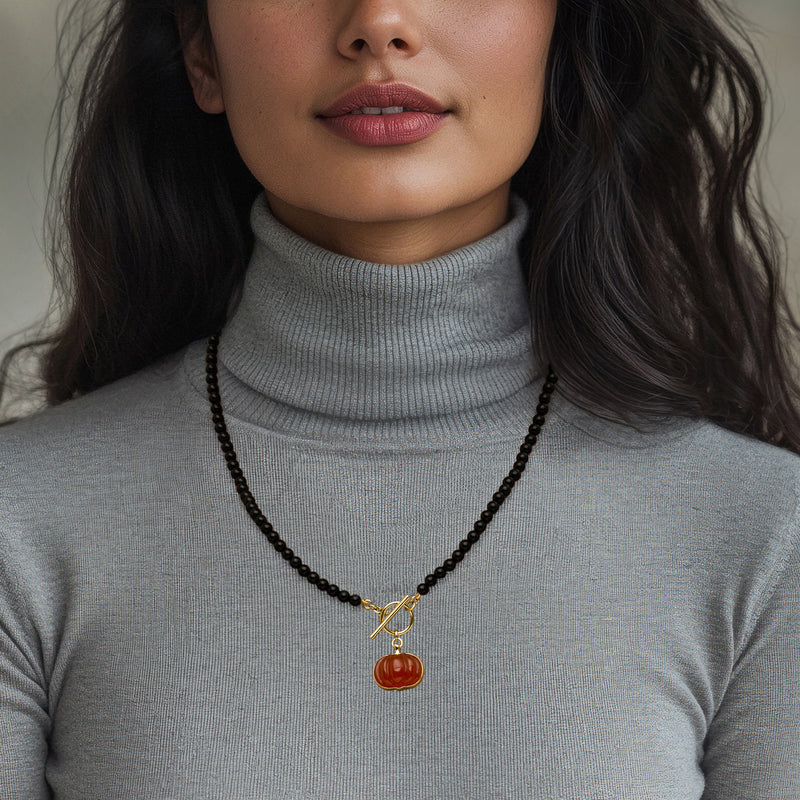 Black bead necklace with gold toggle and orange pumpkin pendant on model