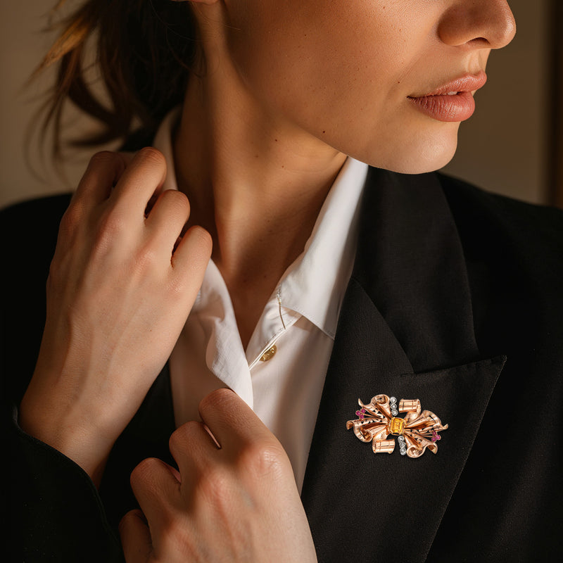 Rose gold bow pin with citrine center and ruby accents on suit lapel
