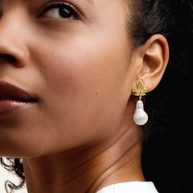 Gold-tone leaf and baroque pearl drop earrings on model's ear
