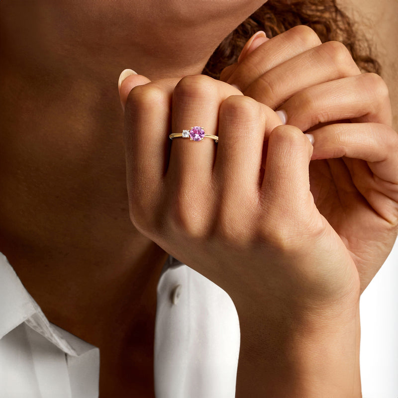 Gold ring with oval pink sapphire and diamond accents, worn on hand
