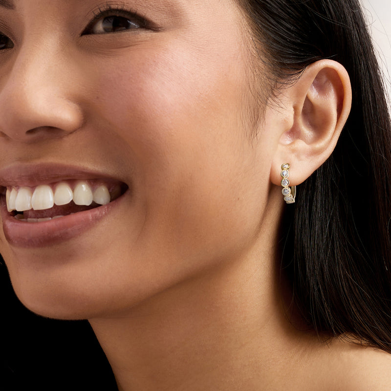 Yellow gold hoop earrings with five bezel-set round diamonds on ear