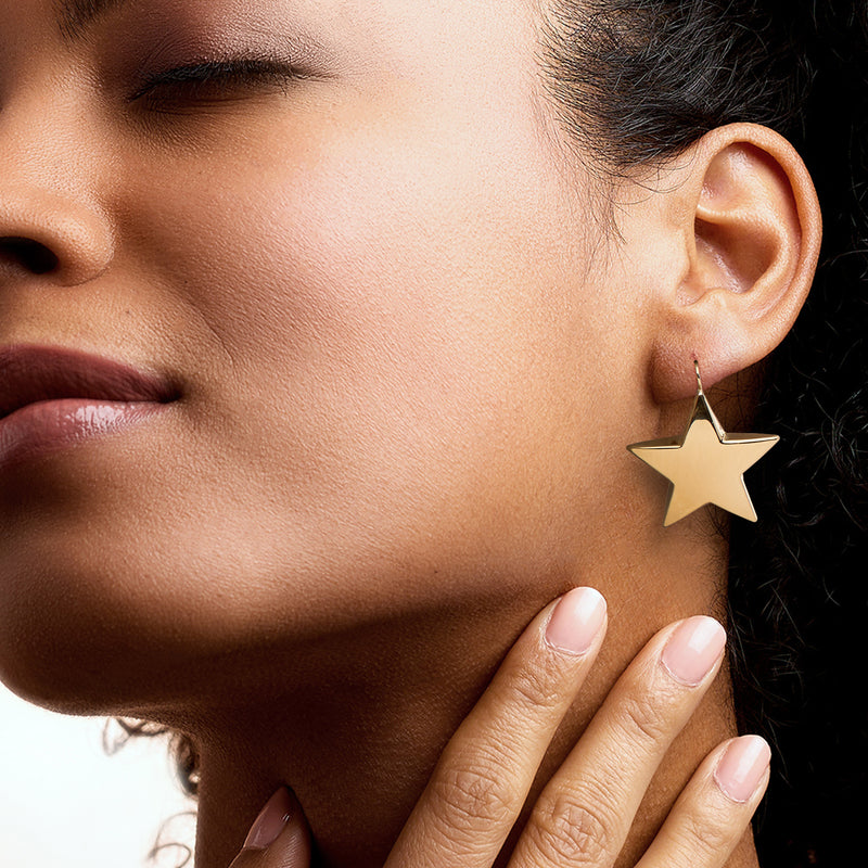 Gold star drop earrings on ear, dangling star on slim earwire