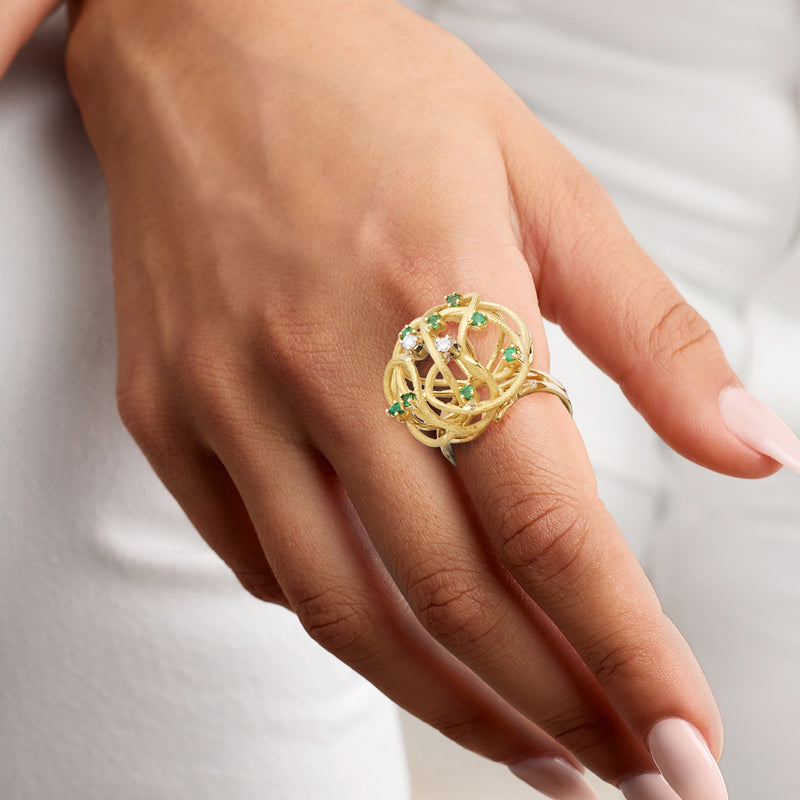 Yellow gold swirl ring with green emerald gemstones and white diamond accents on hand
