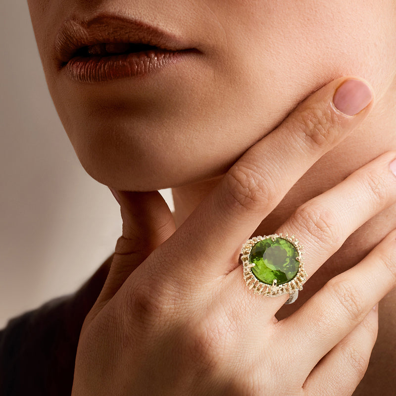 Green peridot ring in 14kt yellow gold worn on a finger, round gemstone halo