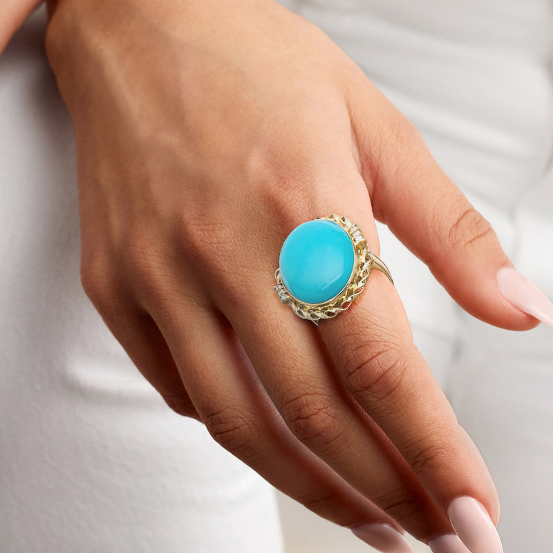 Turquoise oval cocktail ring on hand with ornate 18k yellow gold setting and diamond accents