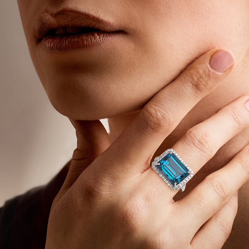 Platinum diamond ring on hand with emerald-cut blue topaz centerpiece