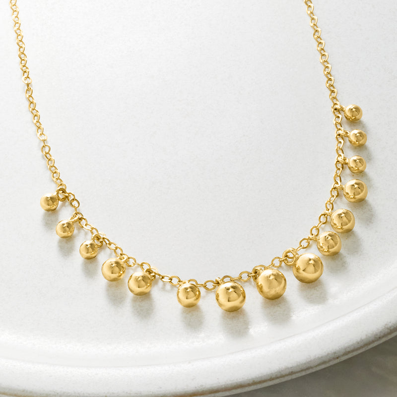 Close-up of graduated round ball bead drop necklace on gold-tone chain