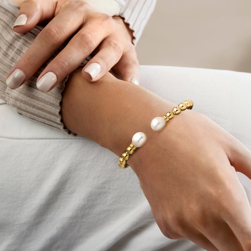 Gold cuff bracelet with ball links and two white cultured pearls on wrist