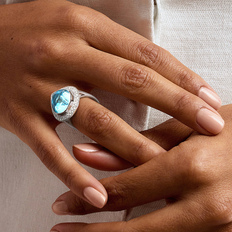 Cocktail ring on hand with blue pear-cut topaz and diamond halo, white gold band