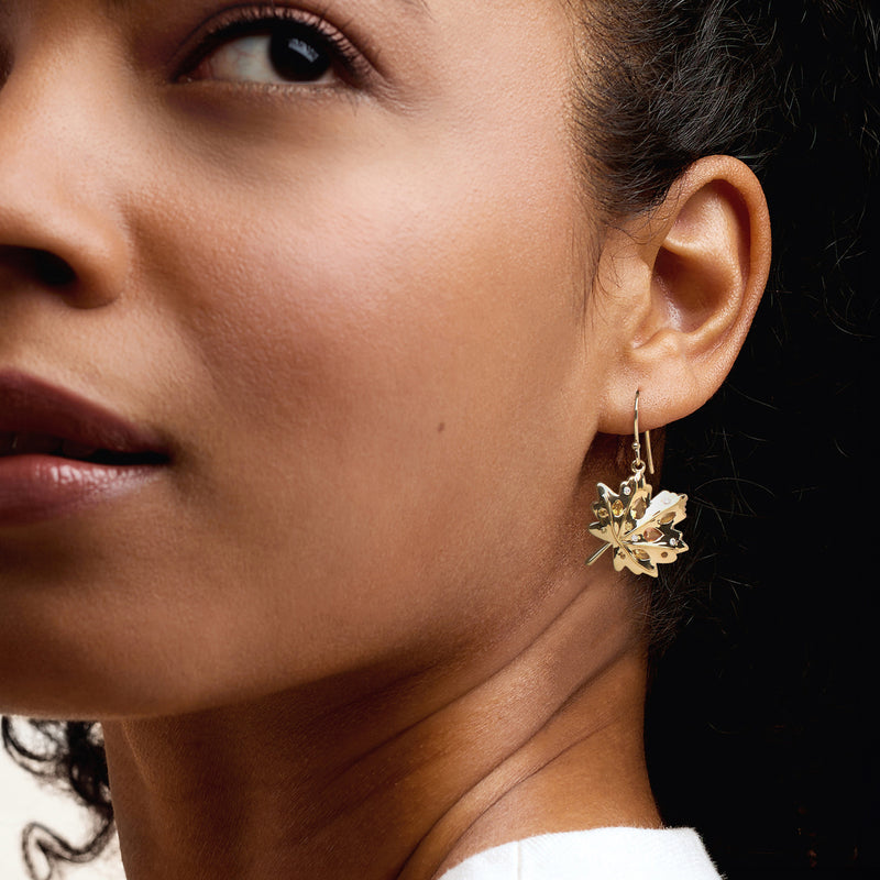 Gold leaf drop earrings with dangling multi-gemstone leaf motif on ear