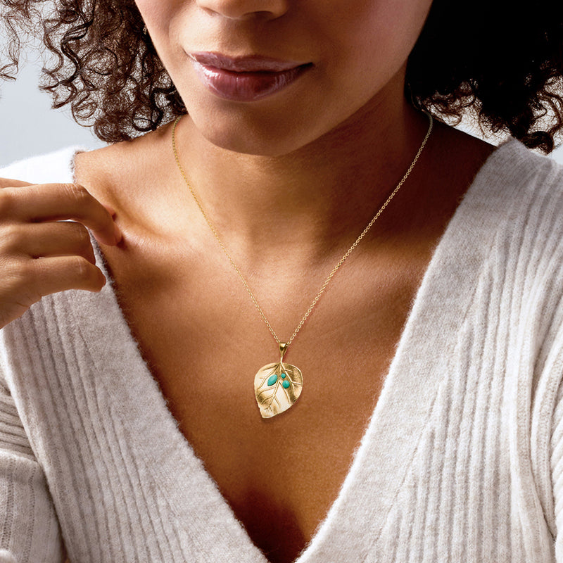 Gold chain leaf pendant necklace with turquoise stones worn at neckline