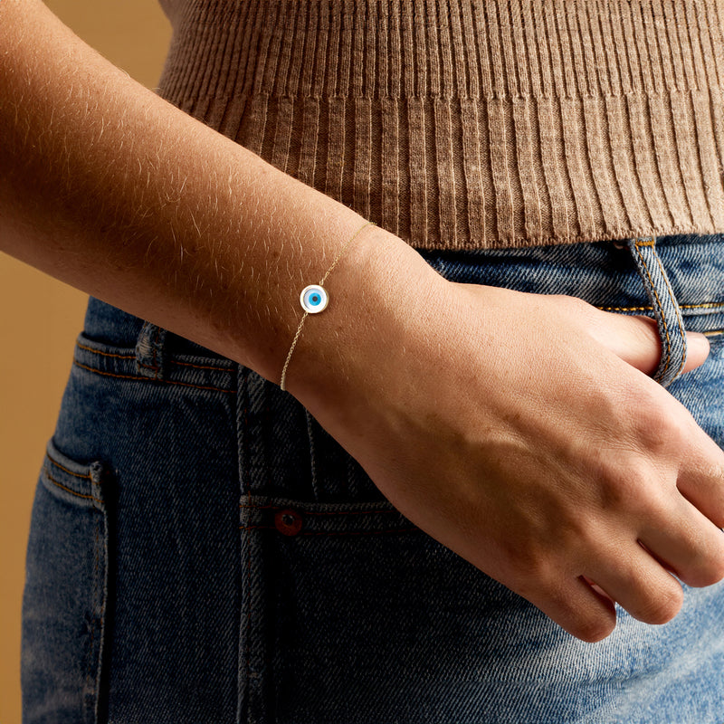 Yellow gold evil eye bracelet on wrist, round blue resin charm with chain