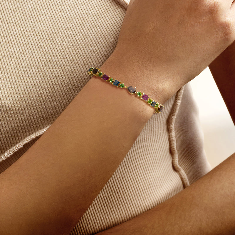 Multi-gemstone tennis bracelet in gold on wrist with small green, purple, blue stones