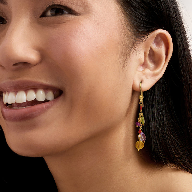 Gold drop earrings with multicolor gemstones, worn on model's ear