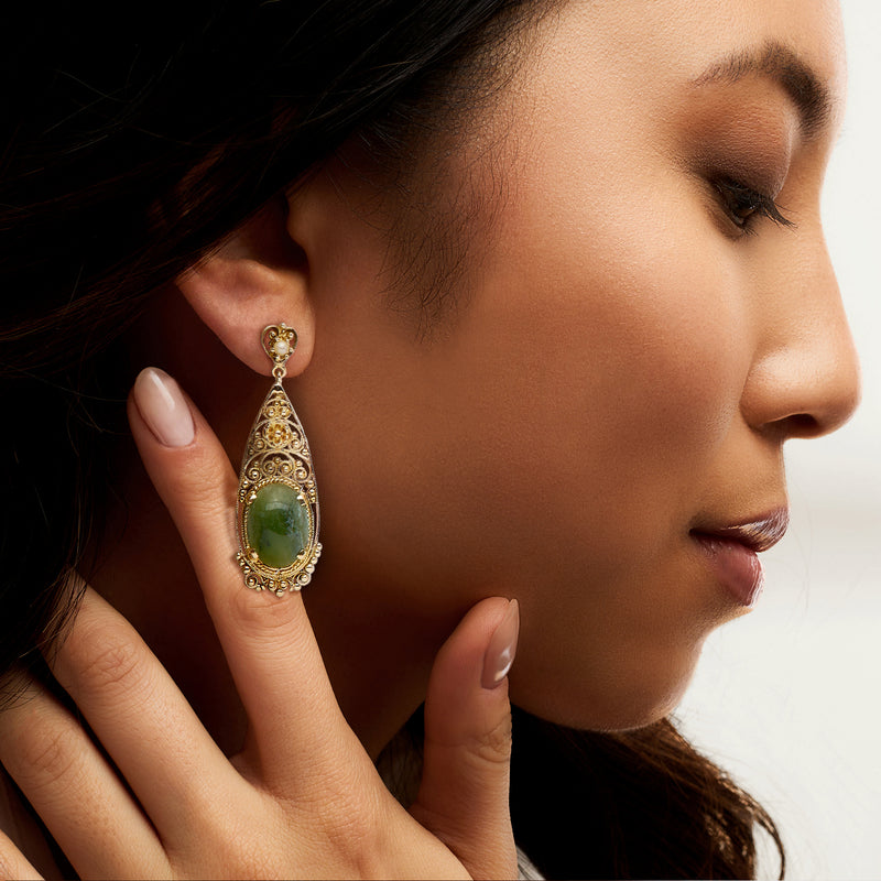 Yellow gold drop earrings with oval green gemstone and ornate frame, worn by model