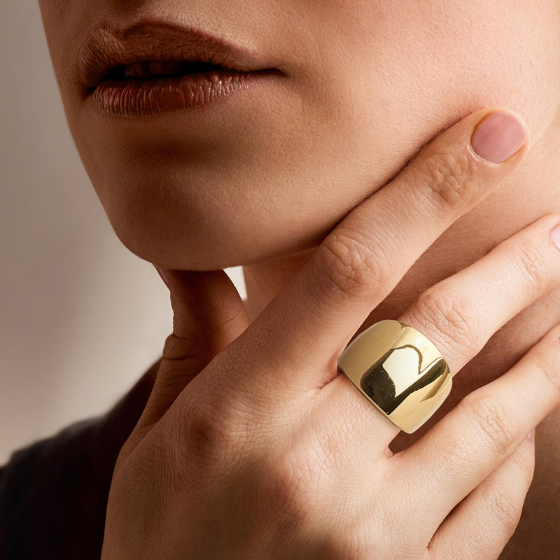 Yellow gold-plated wide dome ring on finger, smooth reflective surface