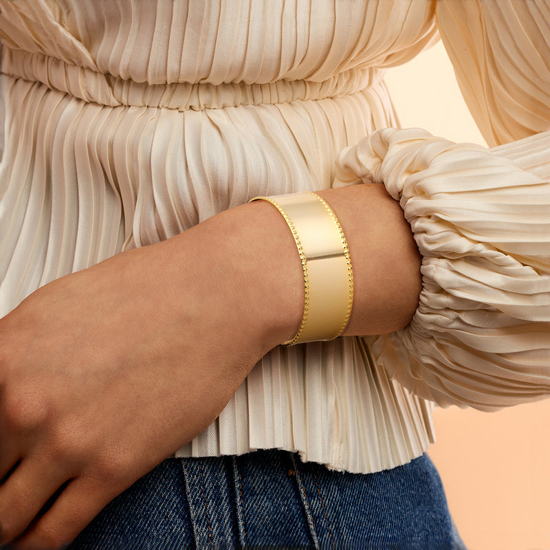 Gold-plated beaded cuff bracelet on wrist, wide polished band