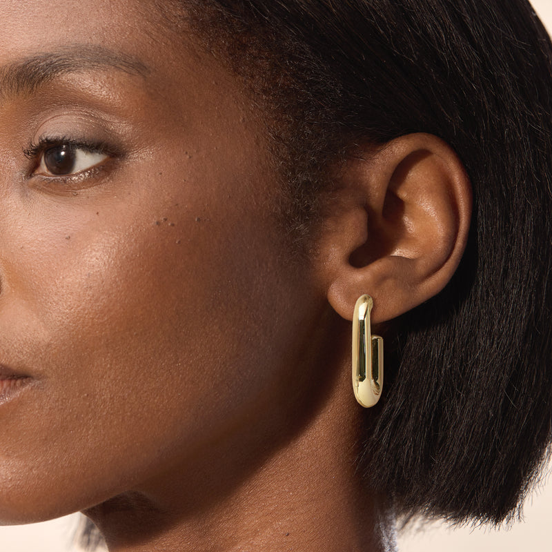 Gold-plated hoop earrings on model ear, linked paper-clip shape, small U profile