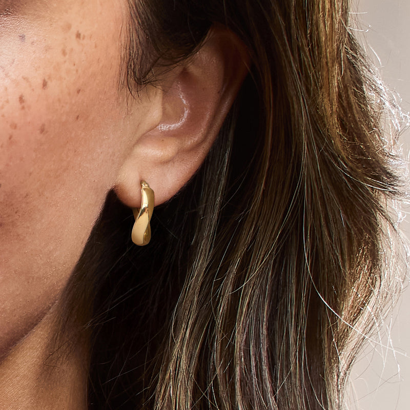 Twisted gold hoop earrings on ear, small hinged hoop with smooth shine