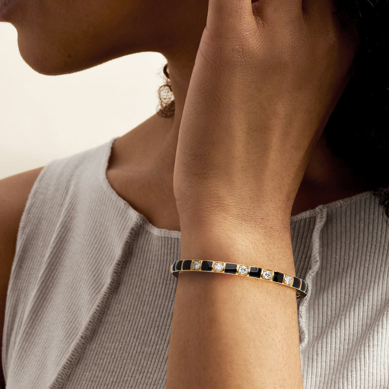 Gold bangle bracelet on wrist with black enamel insets and round diamond accents