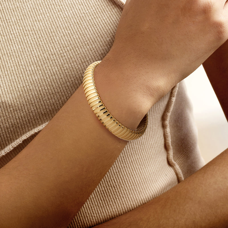 Yellow gold-plated tubogas cuff bracelet on wrist, ribbed tube texture
