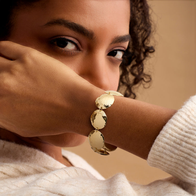 Yellow gold-plated hammered disc bracelet worn on wrist, linked chain with round discs
