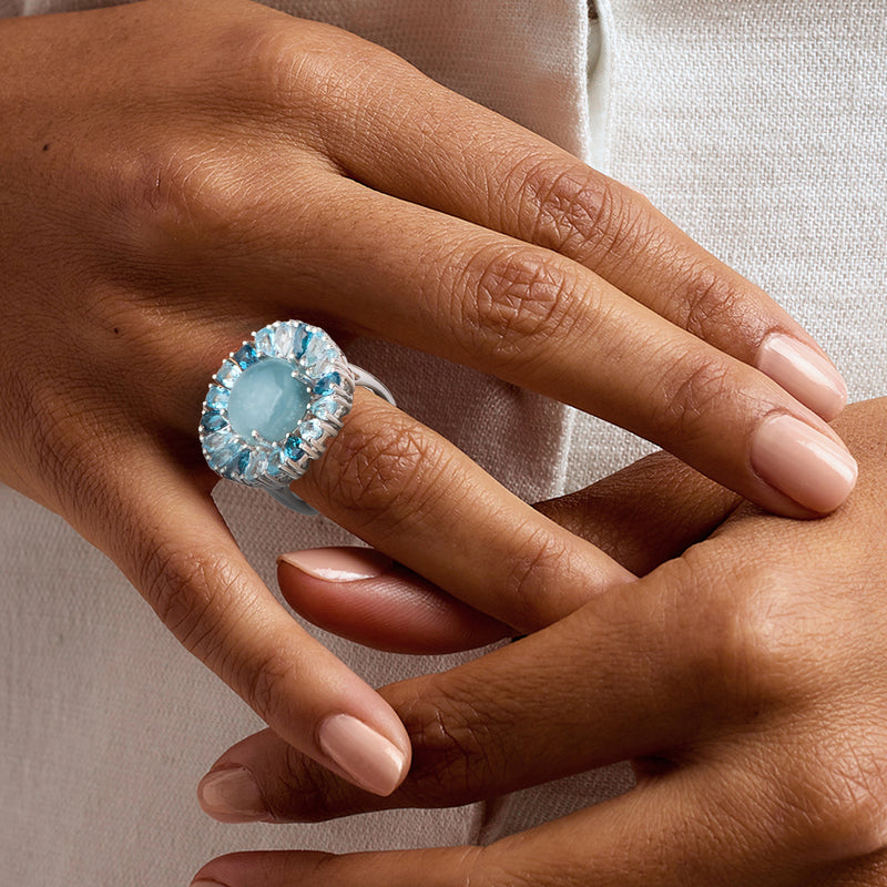 Sterling silver ring with milky blue oval center stone on finger, halo of blue gems
