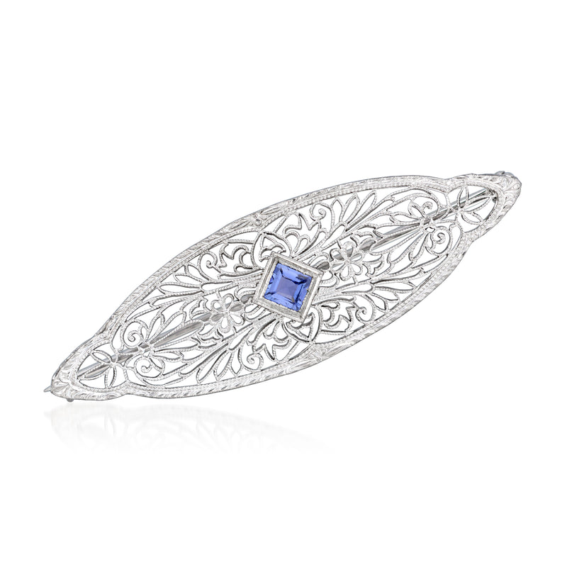 Filigree oval pin in platinum with blue center stone and scrollwork details.