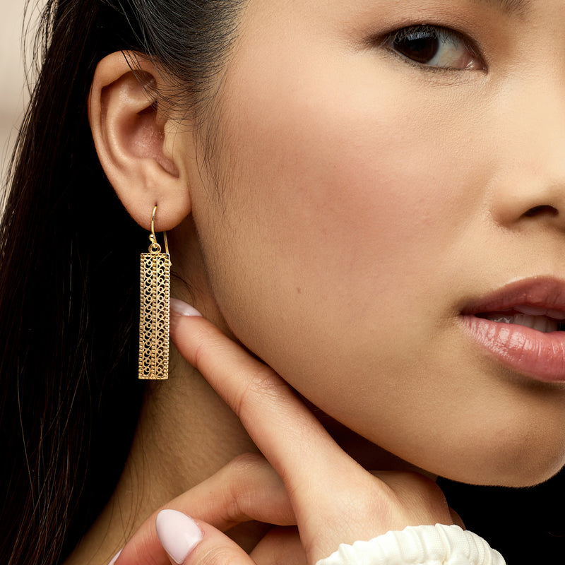 Gold filigree bar drop earrings on ear, close-up of dangling openwork rectangle