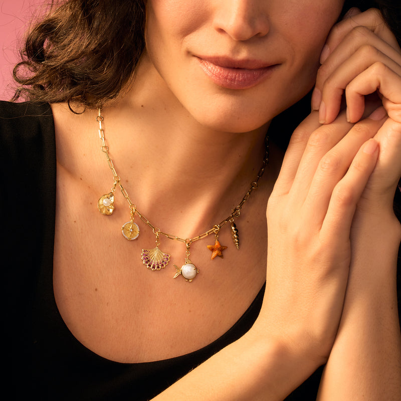 Gold spiral seashell charm on layered necklace with small mixed gold charms