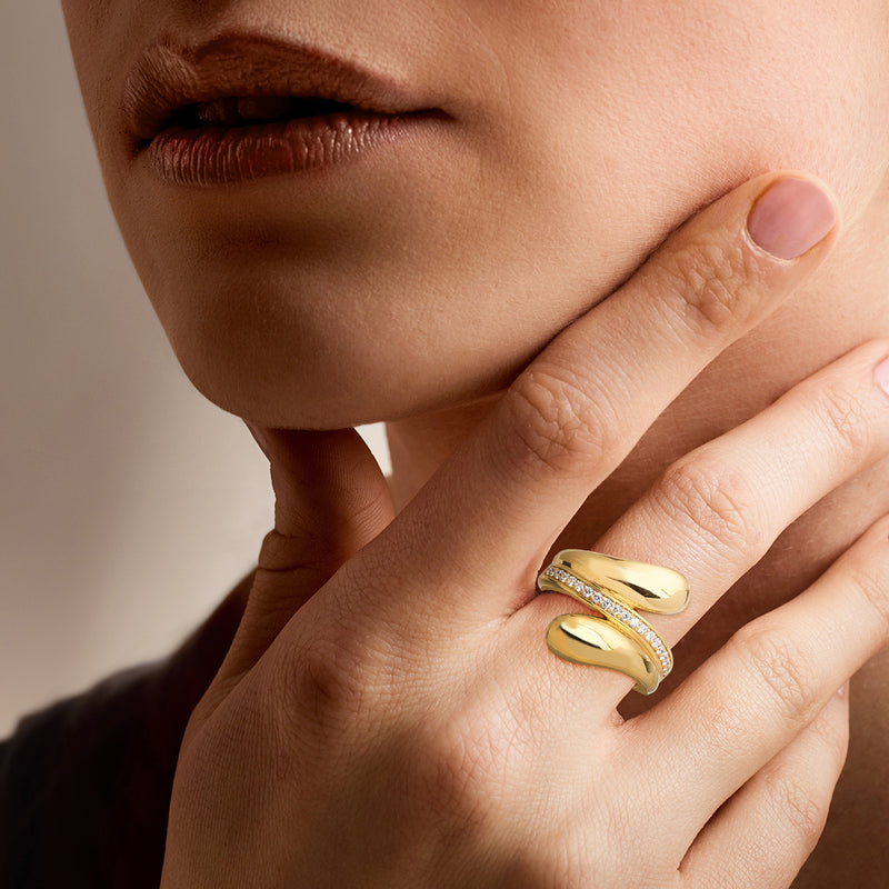 Gold bypass diamond ring on hand, curved polished bands with inset stones