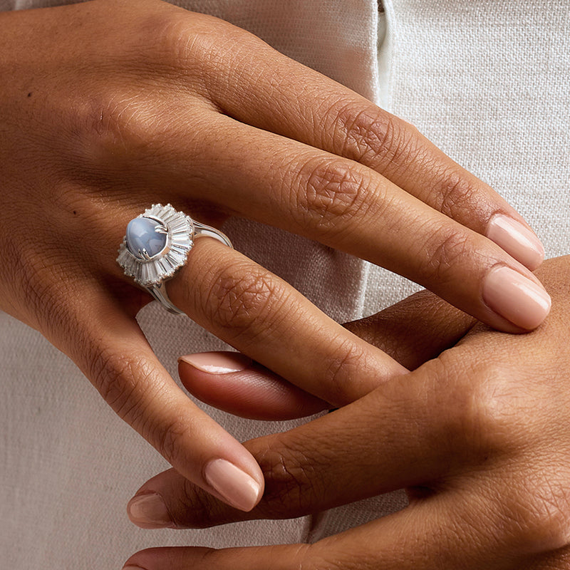 Platinum ring with oval blue star sapphire and diamond halo worn on a finger