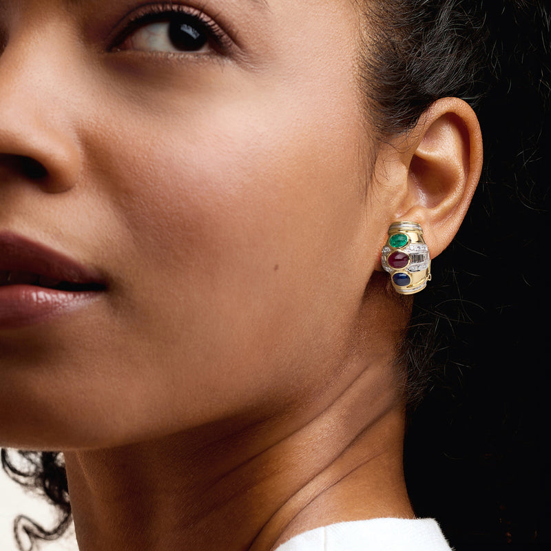 Two-tone gold earrings on ear with green, red, and blue gemstones and diamond halo