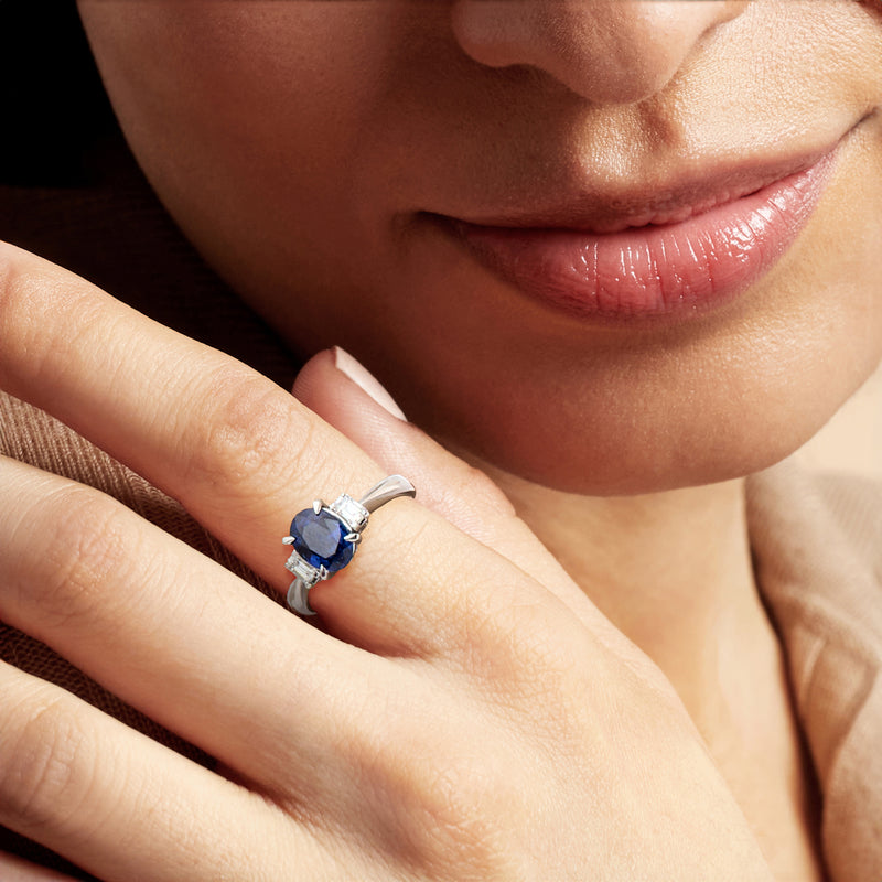 Platinum oval sapphire ring on finger with diamond side stones