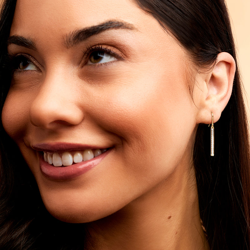 Gold linear bar drop earrings with small diamond rows, worn on model ear