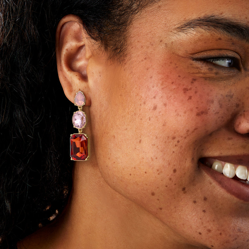 Gold-plated drop earrings on ear: pink oval and red square gemstones