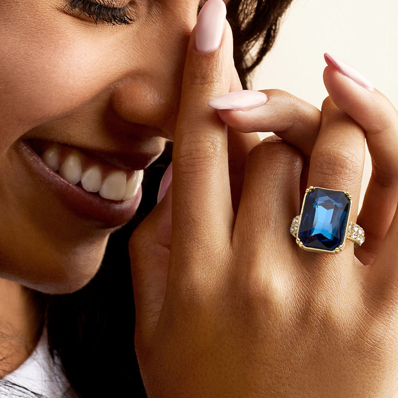 Gold-plated ring on hand with blue square center stone and round CZ halo