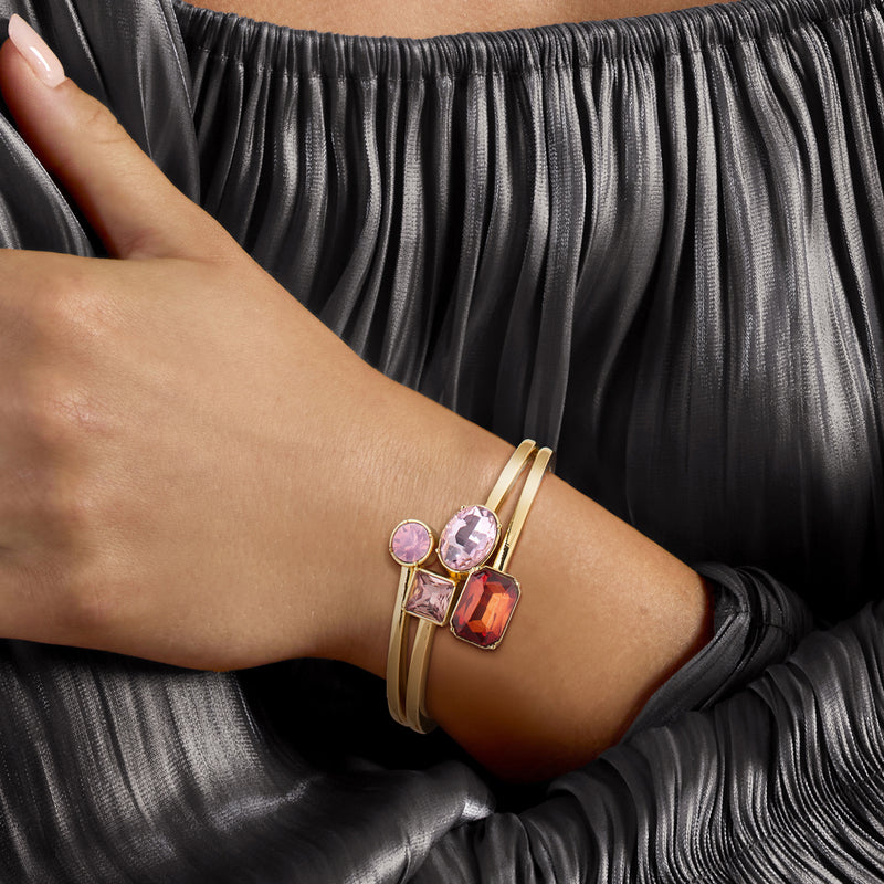 Gold-plated bangle bracelet worn on wrist, pink and red simulated gemstone accents