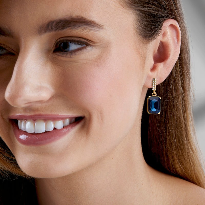 Gold drop earrings with blue square stones and clear CZ details on pierced ears