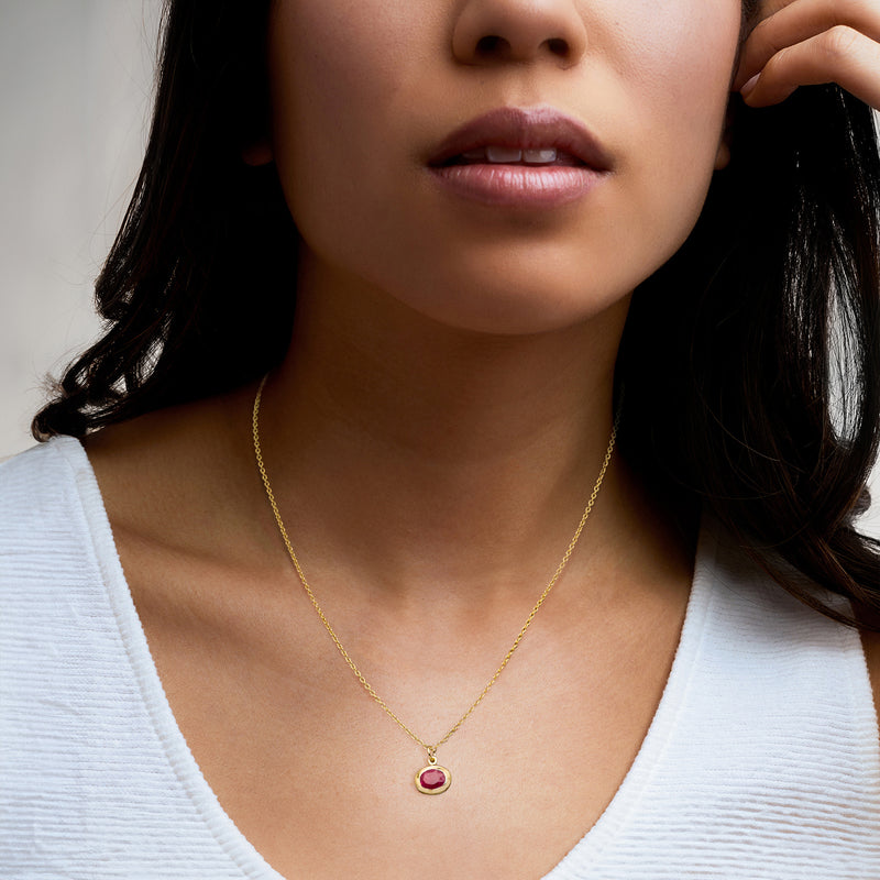 Gold-tone chain necklace with small red oval gemstone pendant on model