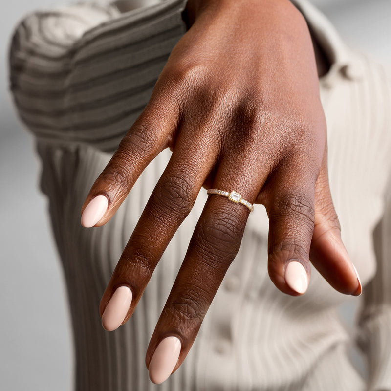 Gold-tone diamond ring on hand with emerald-cut center and round stone band