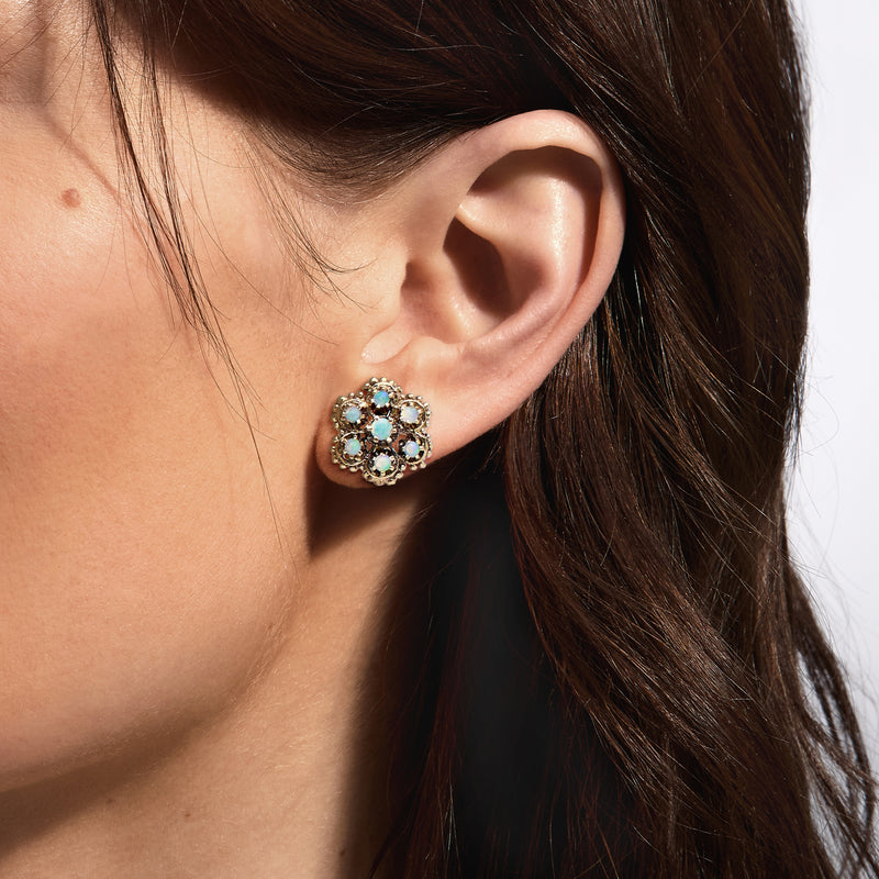 Flower clip earrings on ear with gold setting and blue opal-like stones