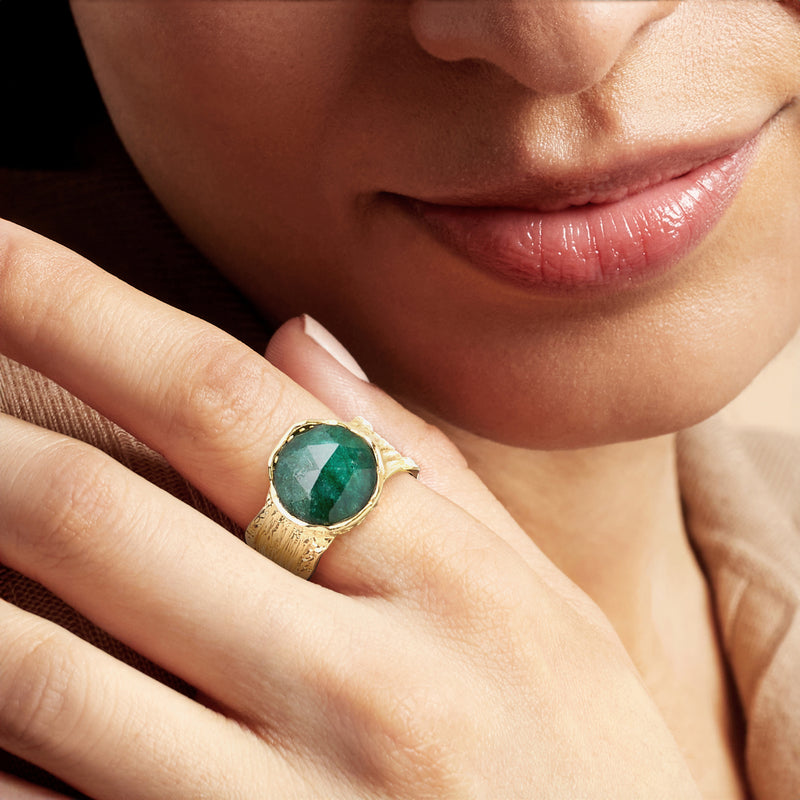 Gold ring with emerald-green oval stone on finger, engraved wide band
