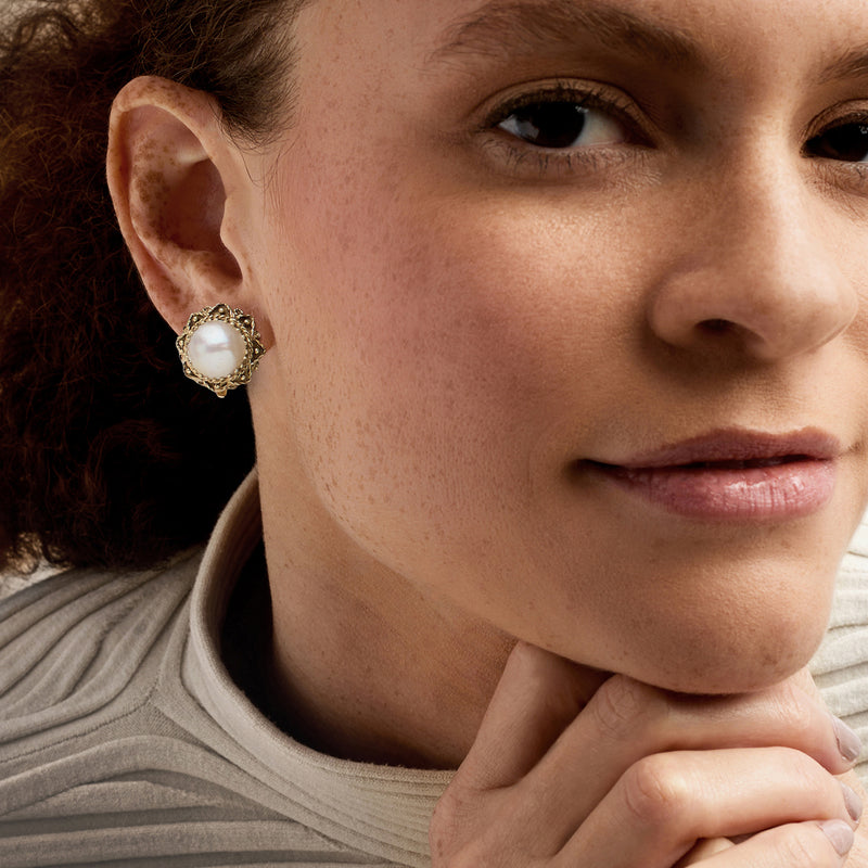 Cultured pearl stud earrings in 14kt yellow gold with ornate frame, worn on ear